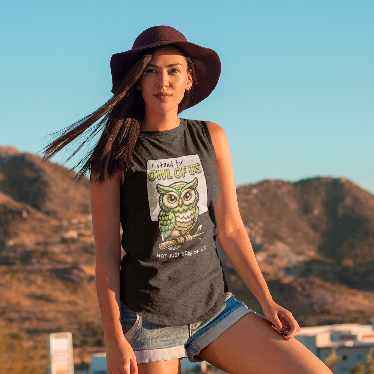 Woman wearing a tank top with an owl graphic and text, standing against a mountainous landscape.