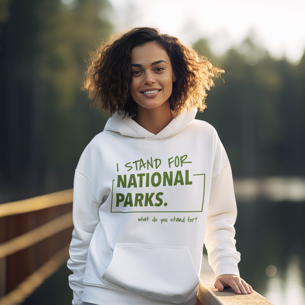 Woman wearing a hoodie with 'I stand for National Parks' text by a lake.
