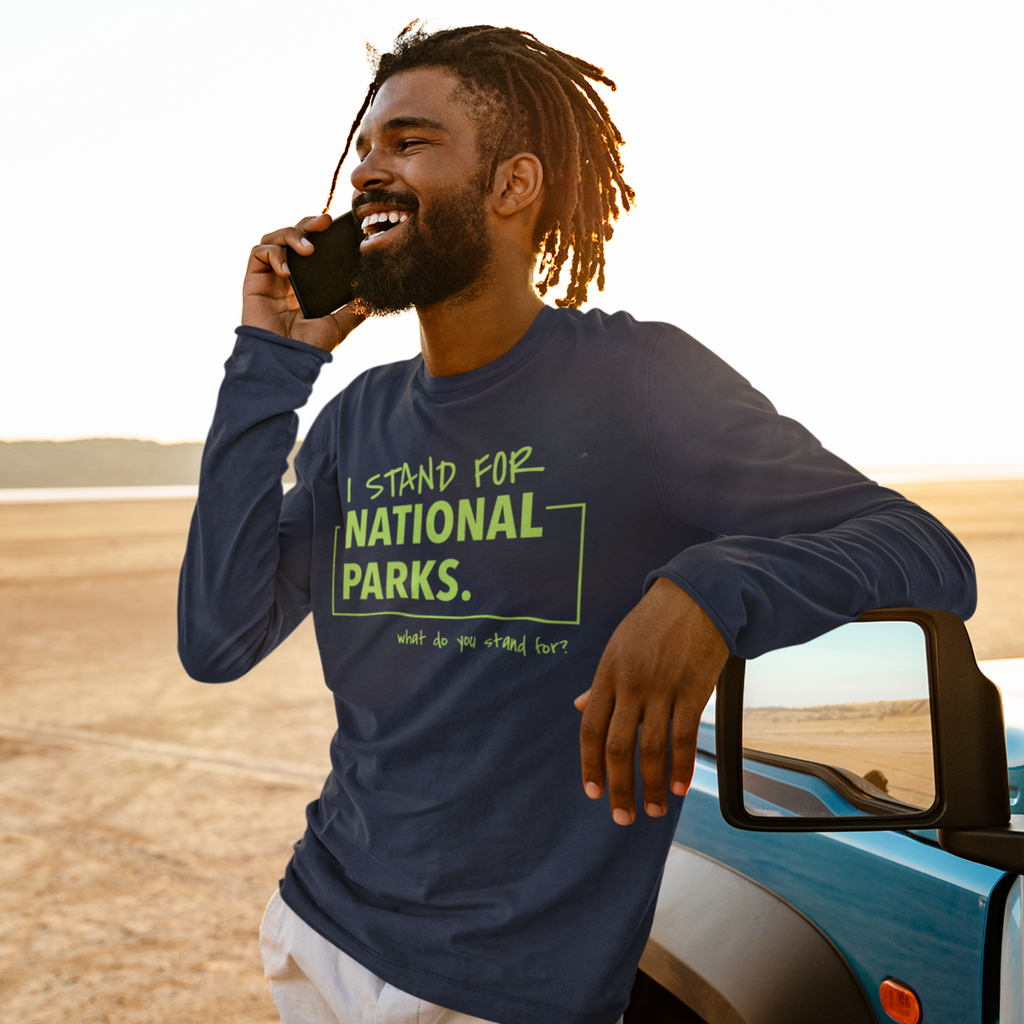 Man in a 'I Stand for National Parks' shirt talking on a phone in a desert setting
