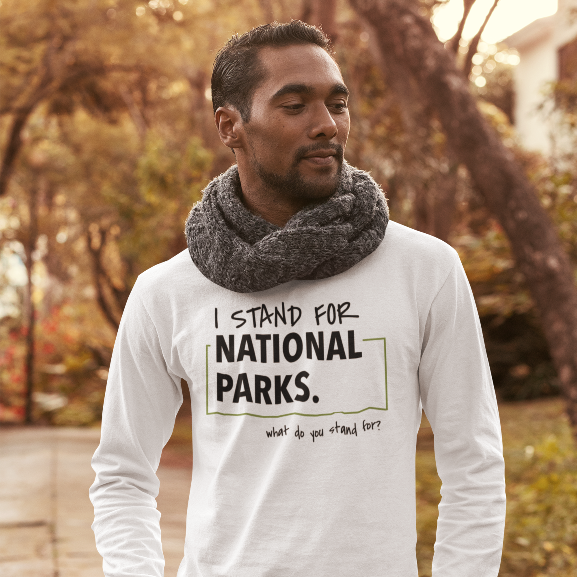 Man wearing a white long-sleeve shirt with 'I Stand for National Parks' text in a park setting.